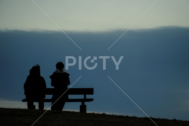 日没の丘のベンチに座る親子
