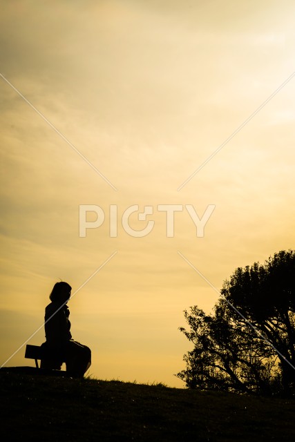 夕焼けの丘に座る女性のシルエット