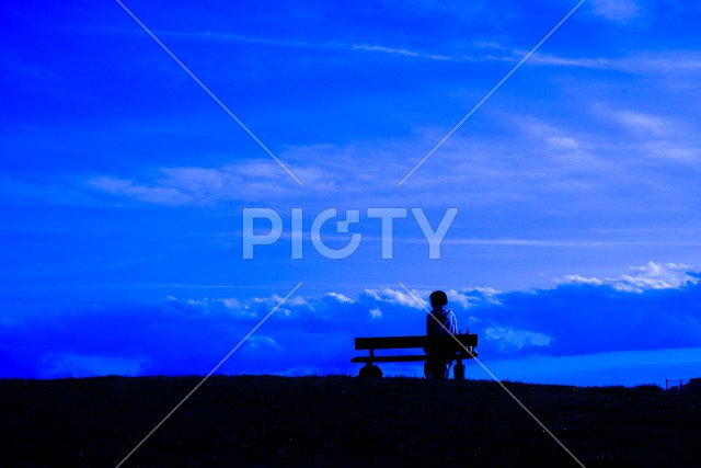 夕焼けの丘に座る女性のシルエットと星空