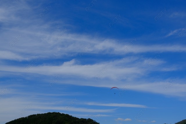 青空と山中を飛ぶパラグライダー
