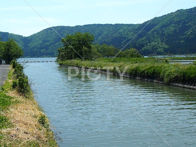 穏やかな湖畔の水路と新緑の山々