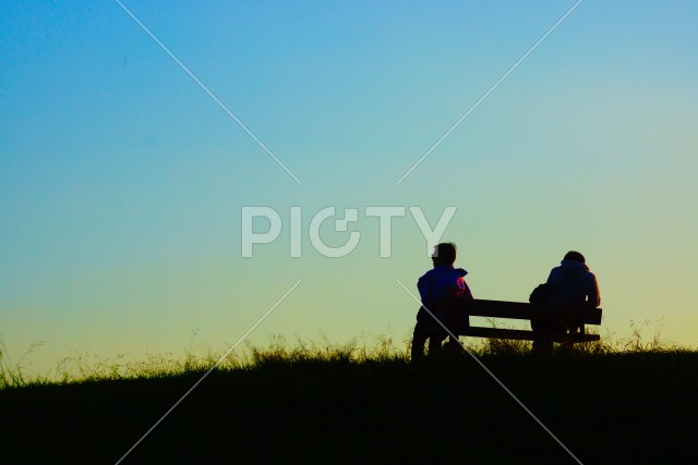 夕暮れの丘でベンチに座る二人