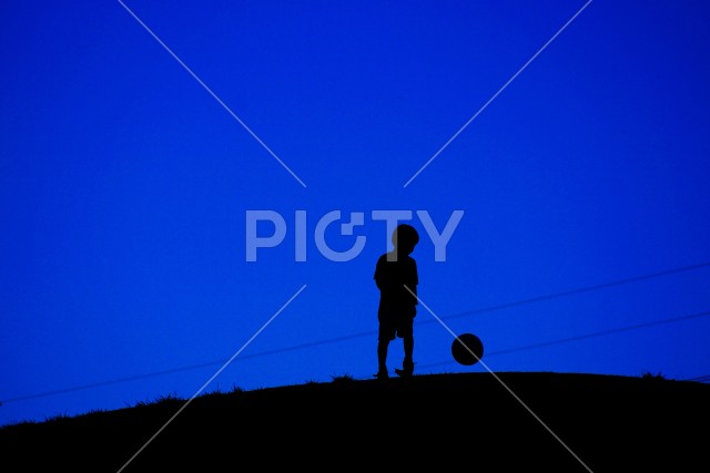サッカーボールで遊ぶ少年（電線あり）