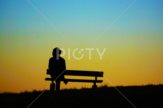 夕暮れの丘のベンチに座る女性