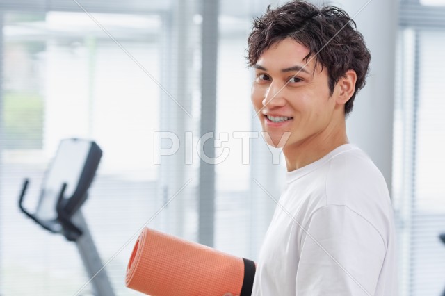 運動施設でヨガマットを持つ笑顔の男性