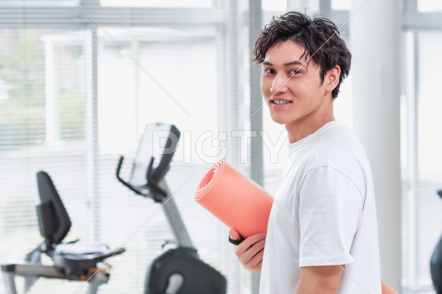 運動施設でヨガマットを持つ笑顔の男性