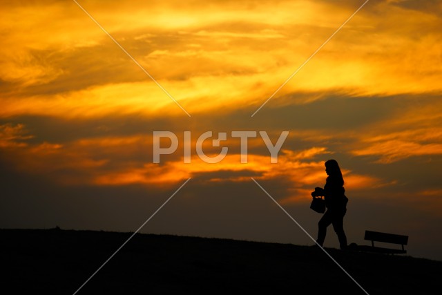 夕暮れの丘を歩く女性